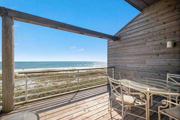 Une terrasse en bois avec une table et des chaises en verre, donnant sur une plage.