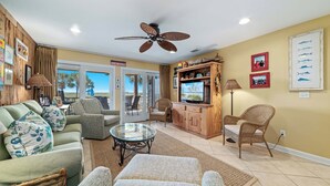 A living room with a ceiling fan, a television, wicker furniture, and a view of the outdoors. - Needle Rush Point C15 | Oceanfront | Walk to FloraBama | Boat Slips | My Beach Getaways (Pensacola)