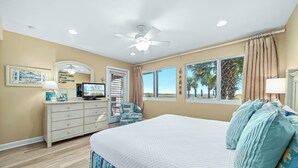 A bedroom with a large bed, a ceiling fan, a dresser, a TV, and a window with a view of palm trees. - Needle Rush Point C15 | Oceanfront | Walk to FloraBama | Boat Slips | My Beach Getaways (Pensacola)