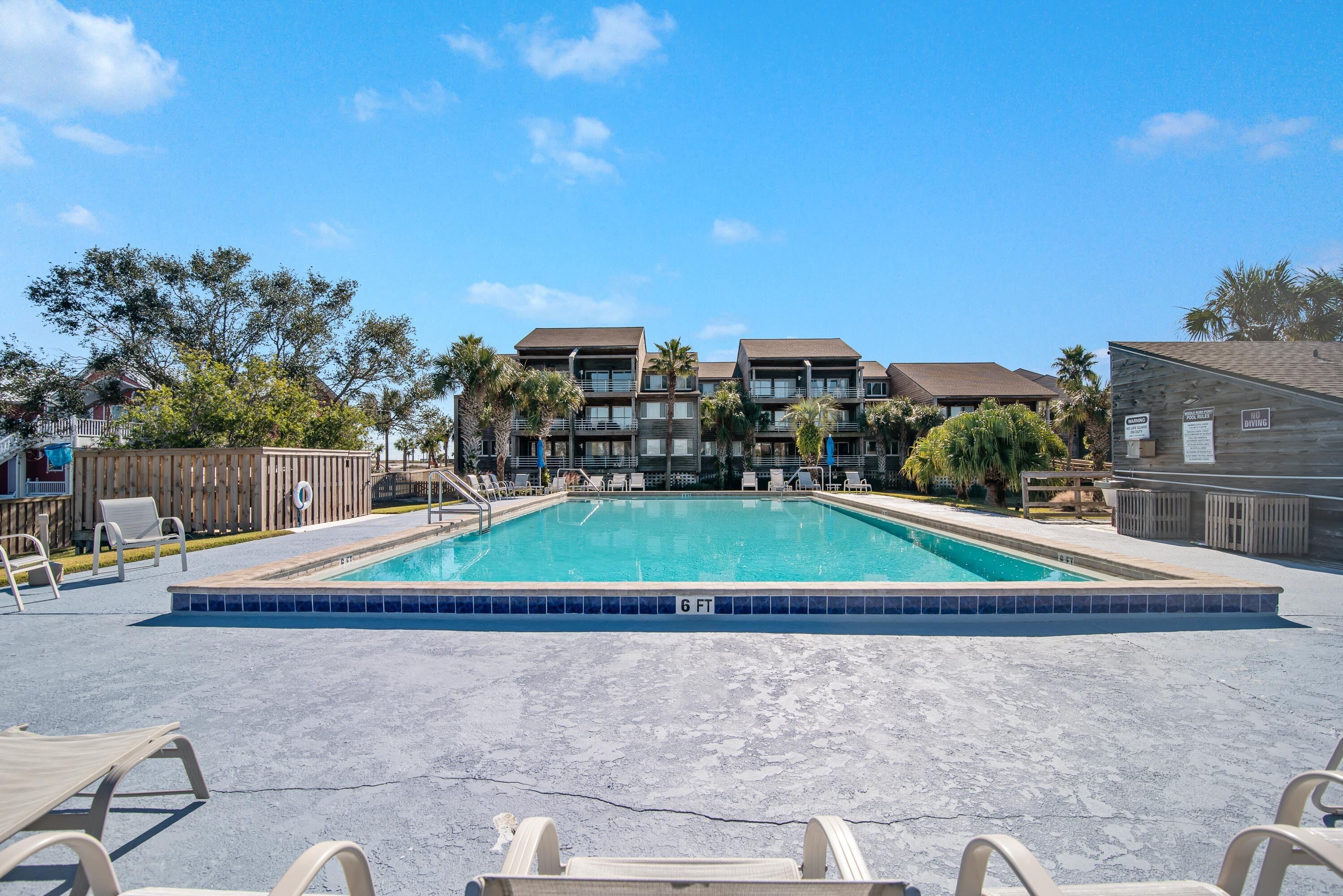 A rectangular swimming pool with a 6 FT depth marking, surrounded by lounge chairs and a wooden deck.