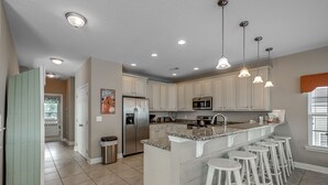 Una cocina moderna con armarios blancos, electrodomésticos de acero inoxidable y una zona de bar con taburetes.