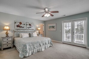 A bedroom with a bed, nightstands, a ceiling fan, and artwork on the walls.