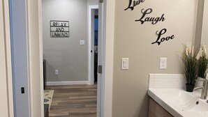 Un pasillo con suelo de madera, un baño con lavabo y tocador blancos, y una pared decorada con frases motivacionales.