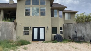 Una casa de dos pisos con puerta principal, varias ventanas y un porche cubierto con sillas.