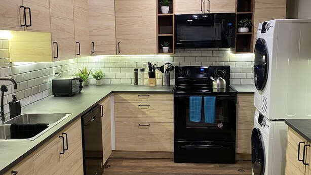 Una cocina moderna con armarios de madera, una estufa negra, un microondas y una lavadora.