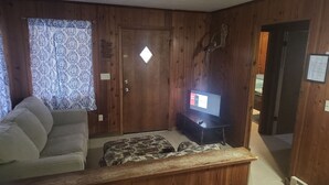 Ein Wohnzimmer mit einer Couch, einem Hocker und einem Fernseher auf einem Schrank.