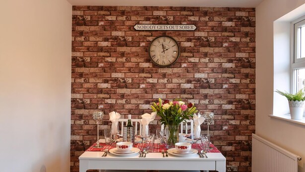 A dining area with a brick wall, a clock, and a table set for two with a vase of flowers. - 2 bedroom accommodation in York (York)