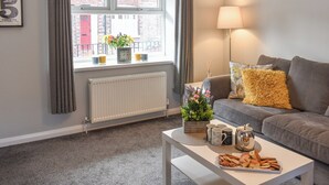 A modern living room with a grey sofa, a white coffee table with snacks, a lamp, and a window with curtains. - 2 bedroom accommodation in York (York)