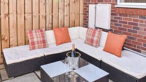 A sectional sofa with white cushions and orange pillows, a glass table with a bottle and glasses, and a brick wall with a window. - 2 bedroom accommodation in York (York)