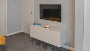 A room with a white wall-mounted TV, a white cabinet with a blue book, and a small candle on the cabinet. - 2 bedroom accommodation in York (York)