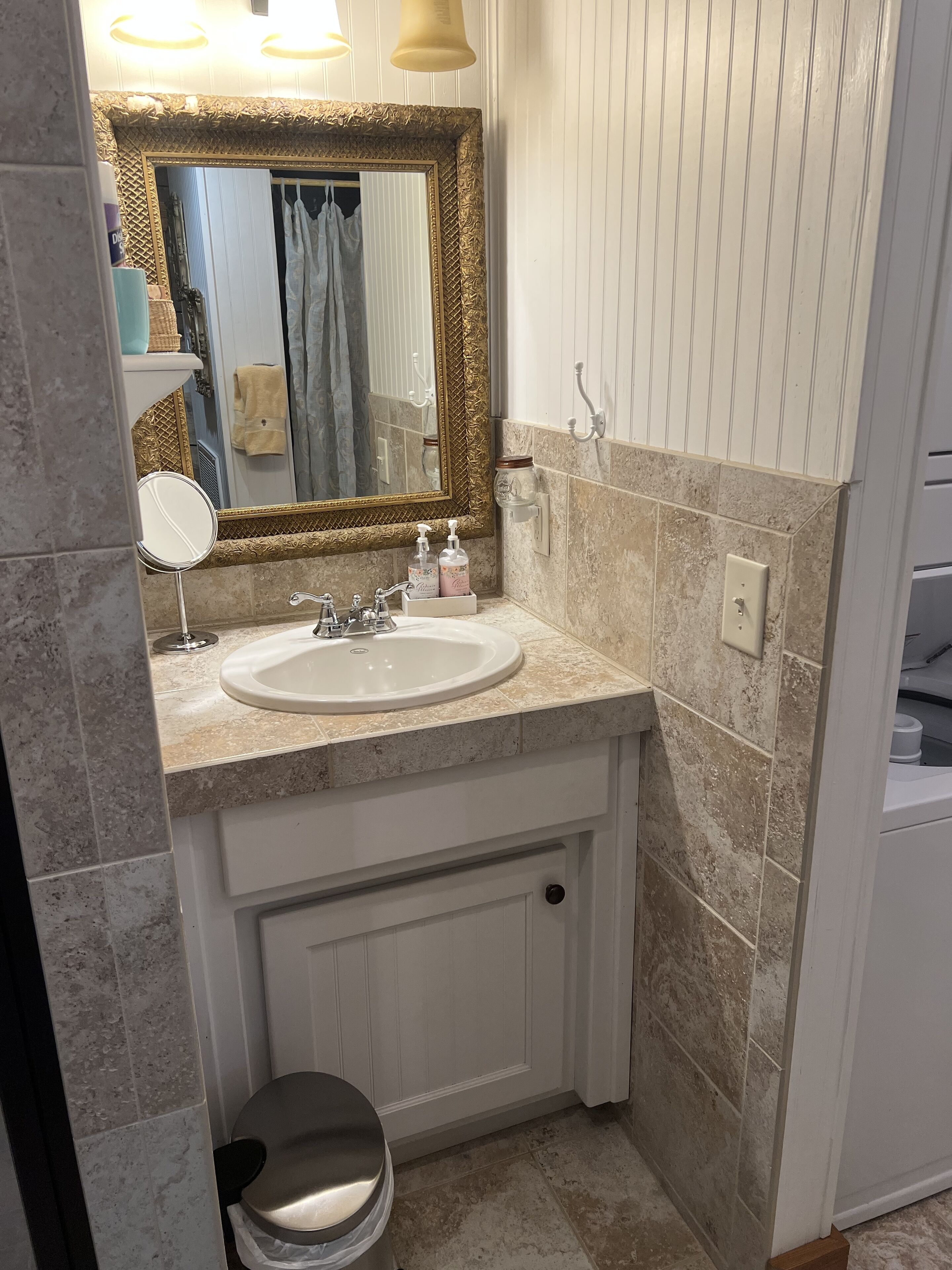 Un baño con un lavamanos blanco, un espejo con marco dorado y un inodoro.