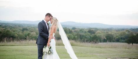 A couple standing on a grassy field with a mountainous backdrop.