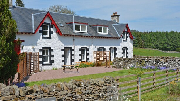 A white farmhouse with a stone wall and a sign indicating '1 & 2 Howpasley Farm Cottages.'
