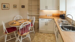 A compact kitchen with white cabinets, a wooden countertop, and a sink. There are two white chairs with red cushions around a small table.
