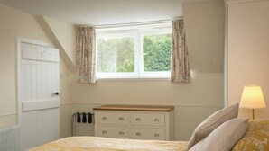 A bedroom with a bed, a dresser, a window with curtains, and a lamp.