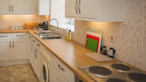 A kitchen with white cabinets, a washing machine, a sink, and a stove.