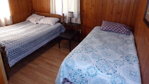 Una habitación con dos camas de madera, una mesita y un ventanal con cortinas.
