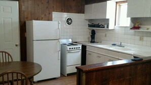 Cocina compacta con refrigerador, estufa y lavamanos. Hay una mesa de comedor de madera y sillas.