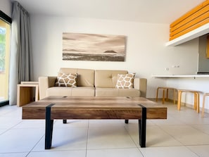 Uma sala de estar moderna com um sofá, uma mesa de centro e uma cozinha ao fundo.