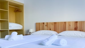 Ein Hotelzimmer mit einem hölzernen Kopfteil, zwei Betten mit weißen Leinen, einem Holzschrank mit gefalteten Handtüchern und einem Nachttisch mit einer Lampe.