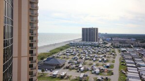 Un hotel de gran altura con vista a una playa, con un estacionamiento lleno de vehículos recreativos y automóviles.
