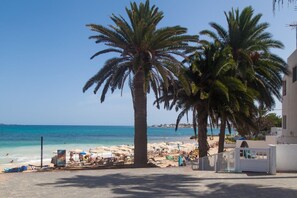 A beach with palm trees, beach chairs, and umbrellas.