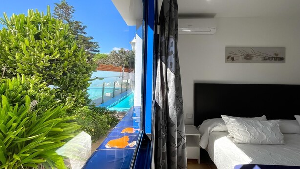 A hotel room with a bed, a small bedside table, and a view of a swimming pool. - Villa Emilia by Best Holidays Fuerteventura (Corralejo)