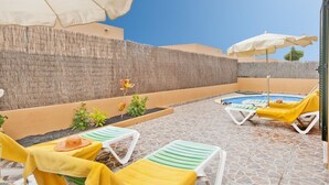 Een zwembadgedeelte met ligbedden en parasols, omgeven door een hoge muur en een heldere lucht.