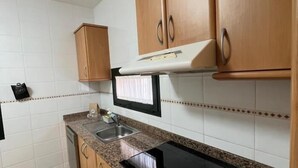 Una cocina con armarios de madera, un lavamanos de acero inoxidable, un microondas y una encimera negra.