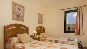 Un dormitorio con dos camas de madera, cada una con una colcha estampada, una mesita de noche con una lámpara y una ventana con cortinas a rayas.