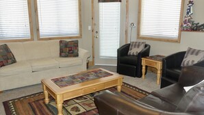 A living room with a white sofa, a black armchair, a wooden coffee table, and a patterned rug. - Ground Level, 2 Bedroom Suite - Close to Village and The Pond!  (Silver Star Mountain)