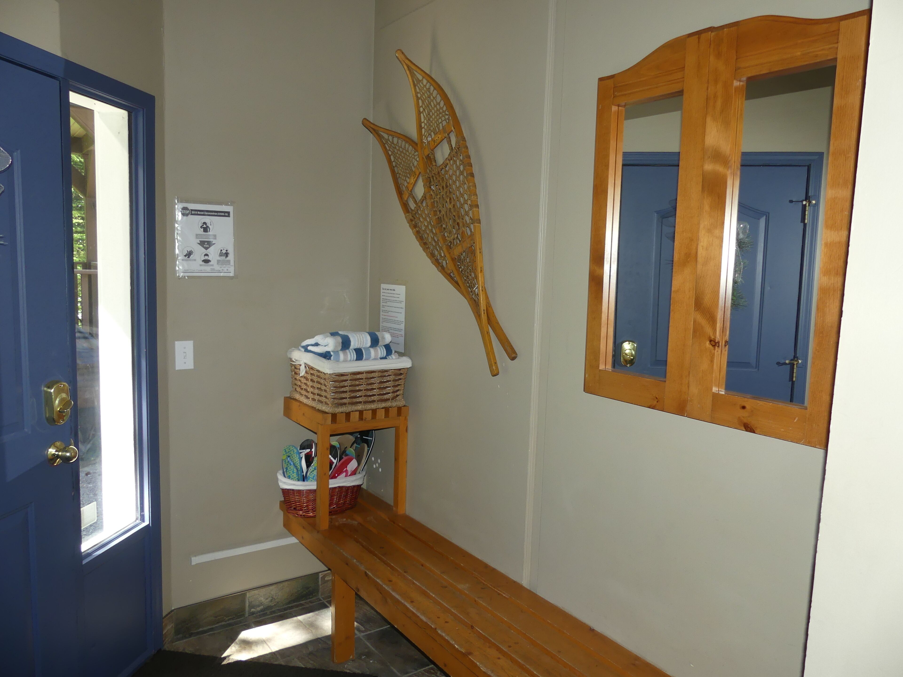 Une salle de bain avec une porte bleue, un banc en bois, un panier en osier et un miroir.