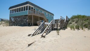 Ett hus vid stranden med en träterrass och en skylt med texten ”STÄNG AV!”.
