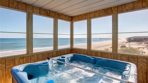 Ett rum med träpanel på väggarna, ett bubbelbad och stora fönster med utsikt över stranden.