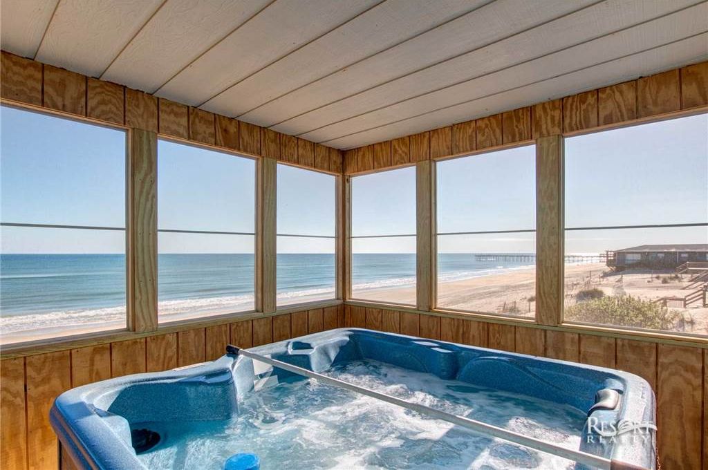 A wooden-paneled room with a hot tub and large windows overlooking the beach.