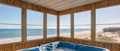 A wooden-paneled room with a hot tub and large windows overlooking the beach.
