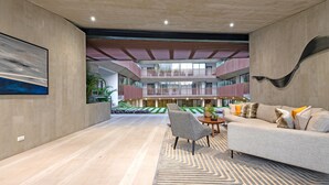 Un espace intérieur vaste et lumineux, doté d’un design moderne, comprenant un grand coin salon avec un canapé et des fauteuils, un tapis à motifs et un grand tableau accroché au mur.