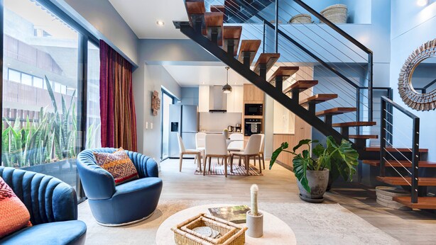 Un salon moderne avec un canapé bleu, une table basse ronde et un escalier à marches en bois.