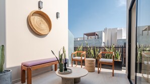 Un espace extérieur moderne aménagé avec un banc, deux chaises, une table ronde et des plantes en pot.