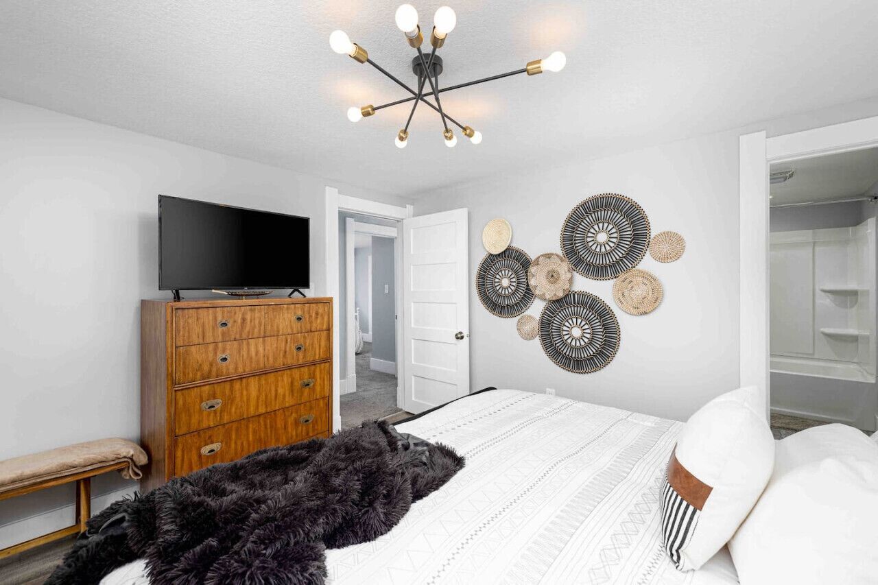 A bedroom with a bed, a wooden dresser, a television, and a wall-mounted light fixture.