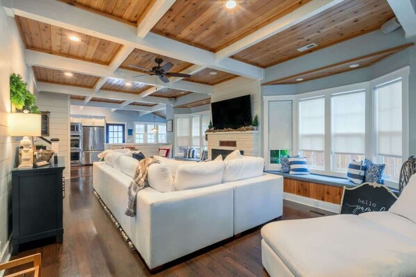 Un salón amplio con sofá blanco, chimenea y ventanas grandes.