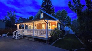 Una casa de dos pisos con porche, fachada de madera y luces colgantes.