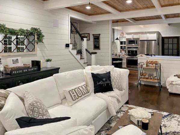 A modern living room with a white sofa, a staircase, and a kitchen area. - Luxury Historic Cottage w/ Chef's Kitchen Downtown (Coeur d'Alene)