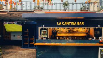Un bar appelé « LA CANTINA BAR », avec un comptoir, des étagères remplies de bouteilles et un espace réservé aux clients, avec des tables et des chaises.