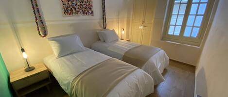 A bedroom with two beds, a nightstand, a wall art piece, a window, and a door.