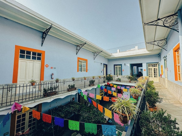Un patio con balcón, plantas en macetas y banderas coloridas.