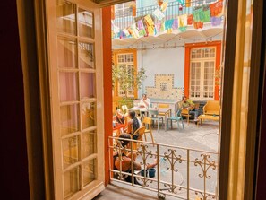 Puerta abierta a un patio con banderas coloridas, mobiliario exterior y una pared de azulejos con diseño geométrico.