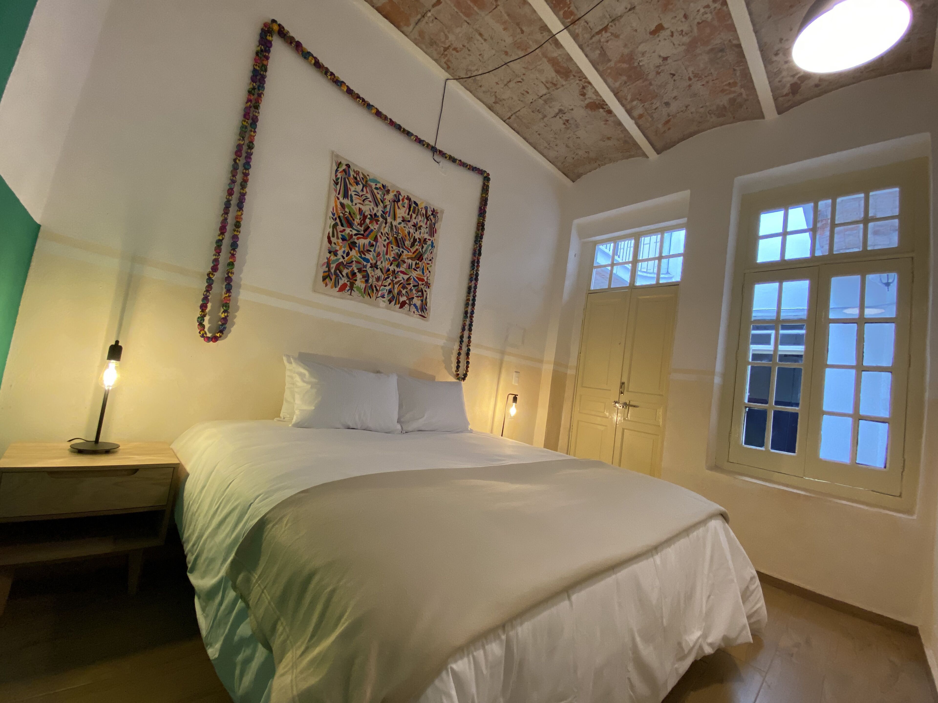 Un dormitorio con una cama grande, una mesita de noche con lámpara, una obra de arte en la pared y una ventana con vistas al exterior.