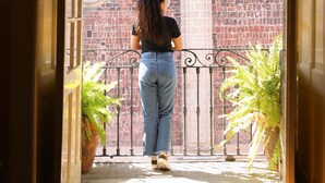 Una mujer parada sobre una cubierta de madera con vista a un edificio de ladrillo a través de una cortina verde.