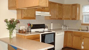 A kitchen with wooden cabinets, a stove, a dishwasher, and two bar stools.
